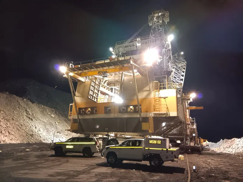 Marquee service vehicles beside a floodlit dragline at night